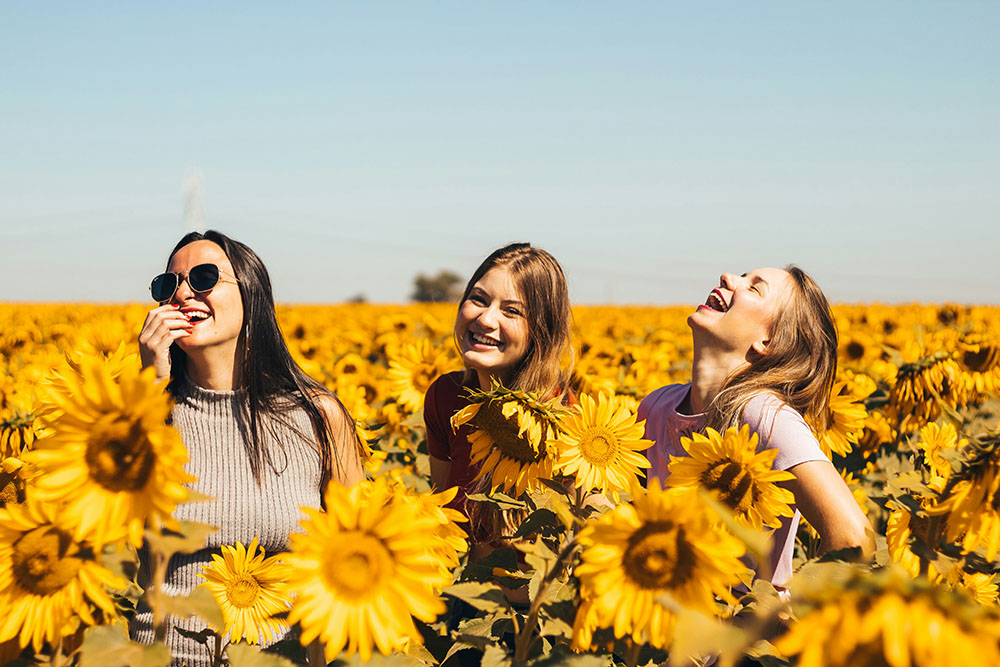 Three girls spending time outside in a sunflower field.