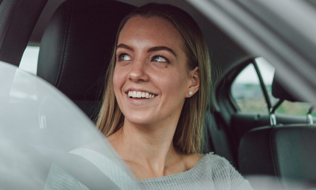 Blond woman looking out the window in the driver's seat of a car.