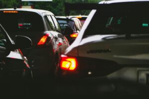 A line of cars stuck in traffic with brake lights glowing in the early evening, captured from a rear-angle view.