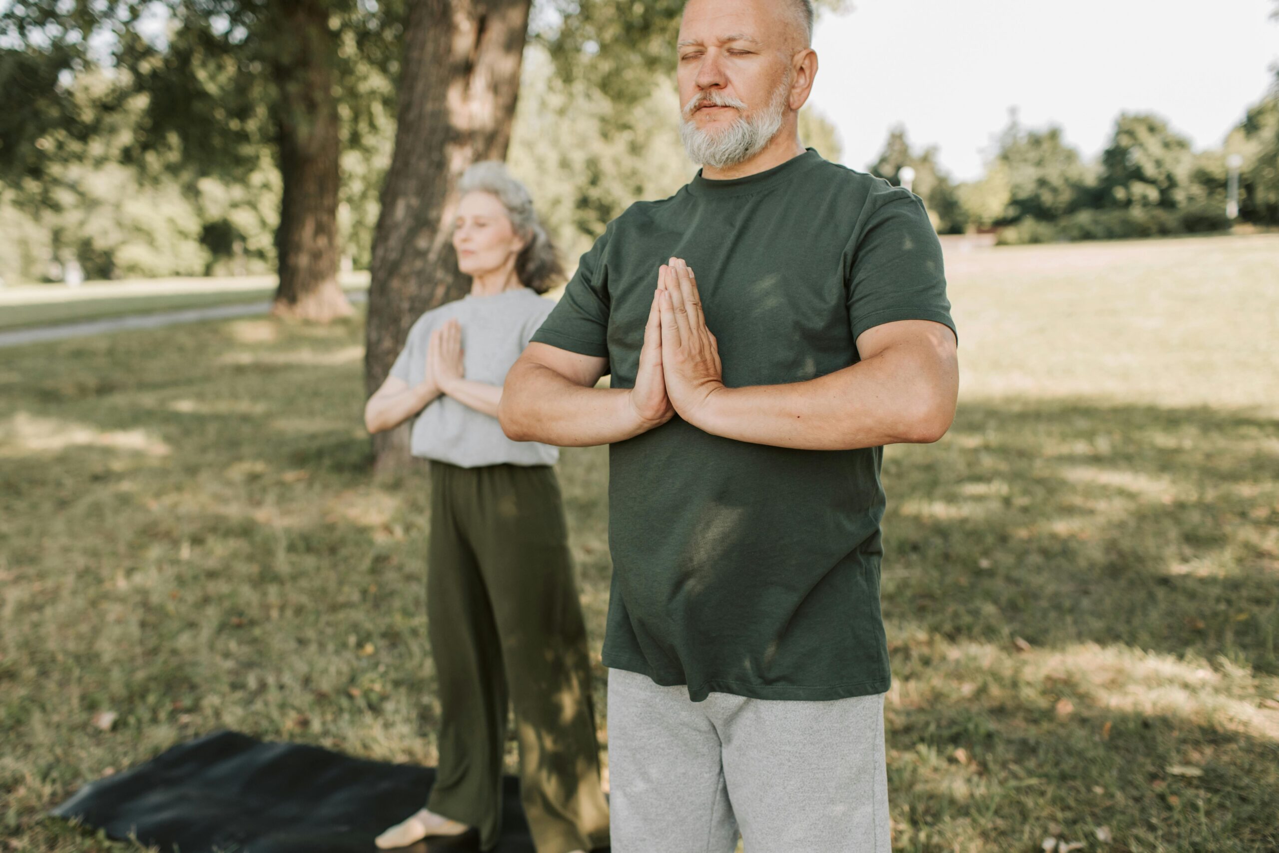 Two older people doing yoga in the park.