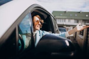 Woman smiling while sitting in her car, suggesting confidence and satisfaction with reduced car insurance premiums.