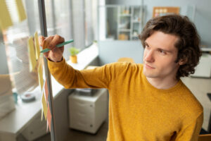 Young man in a mustard sweater analyzing sticky notes on a glass wall, symbolizing careful planning to avoid debt relief pitfalls.